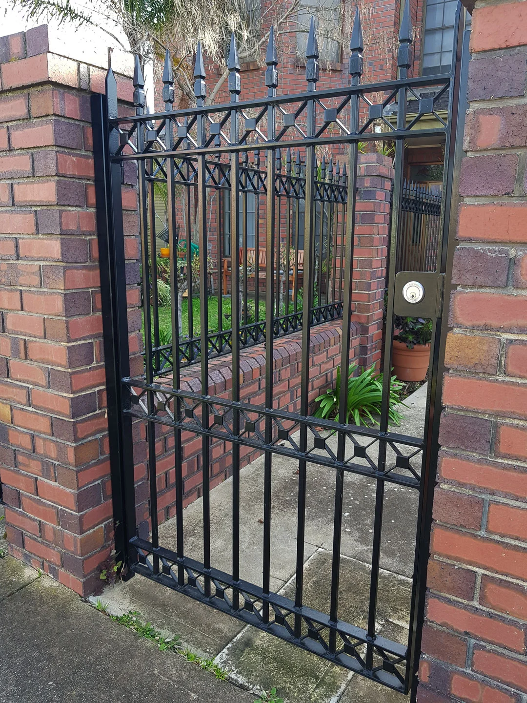 Black steel pedestrian gate set into a brick fence